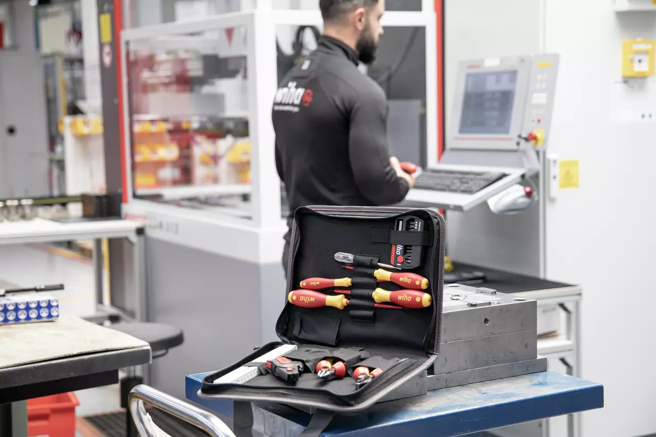Open tool kit with various screwdrivers, in front of a person operating a machine