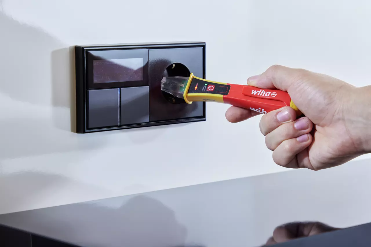 Hand using a red and yellow voltage detector on a black wall socket.