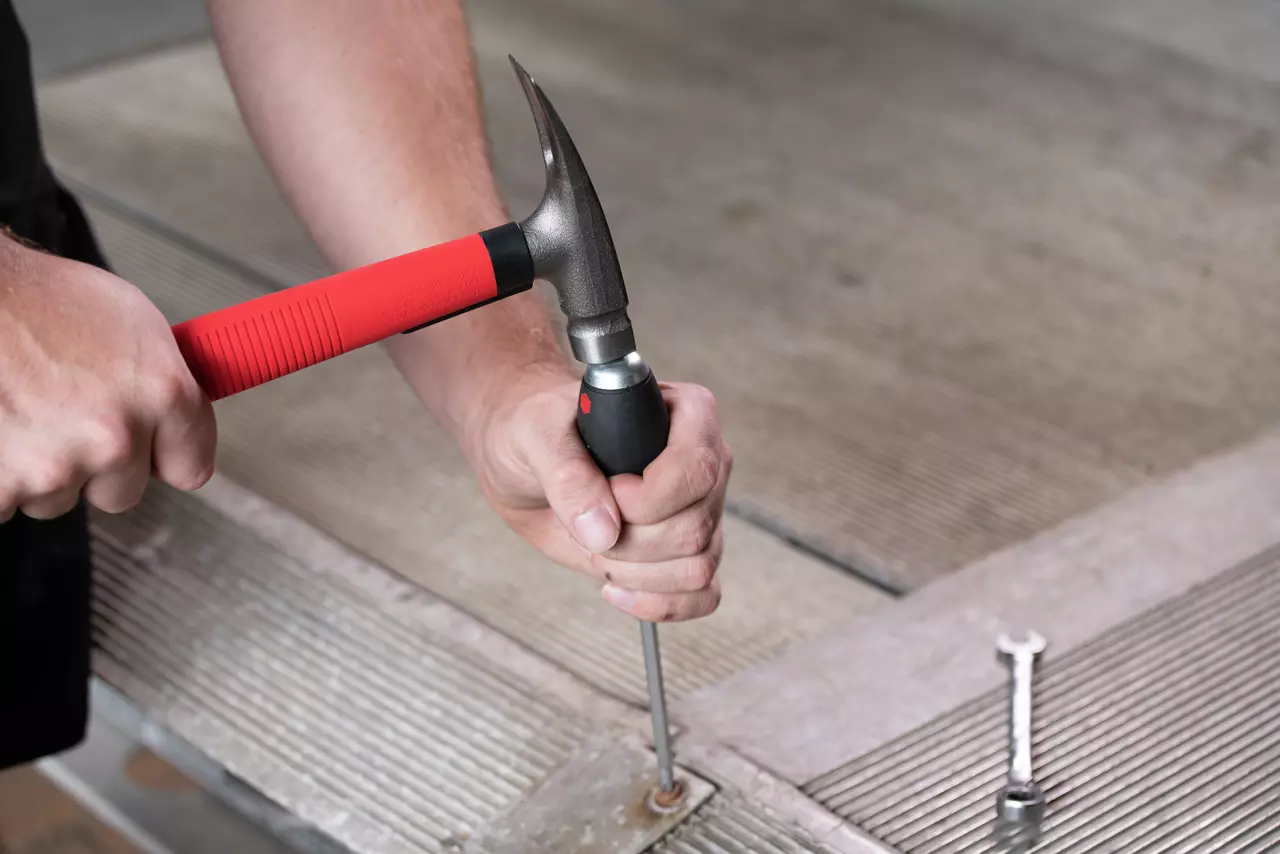 A person using a hammer on a screwdriver with a black handle on a metal surface.