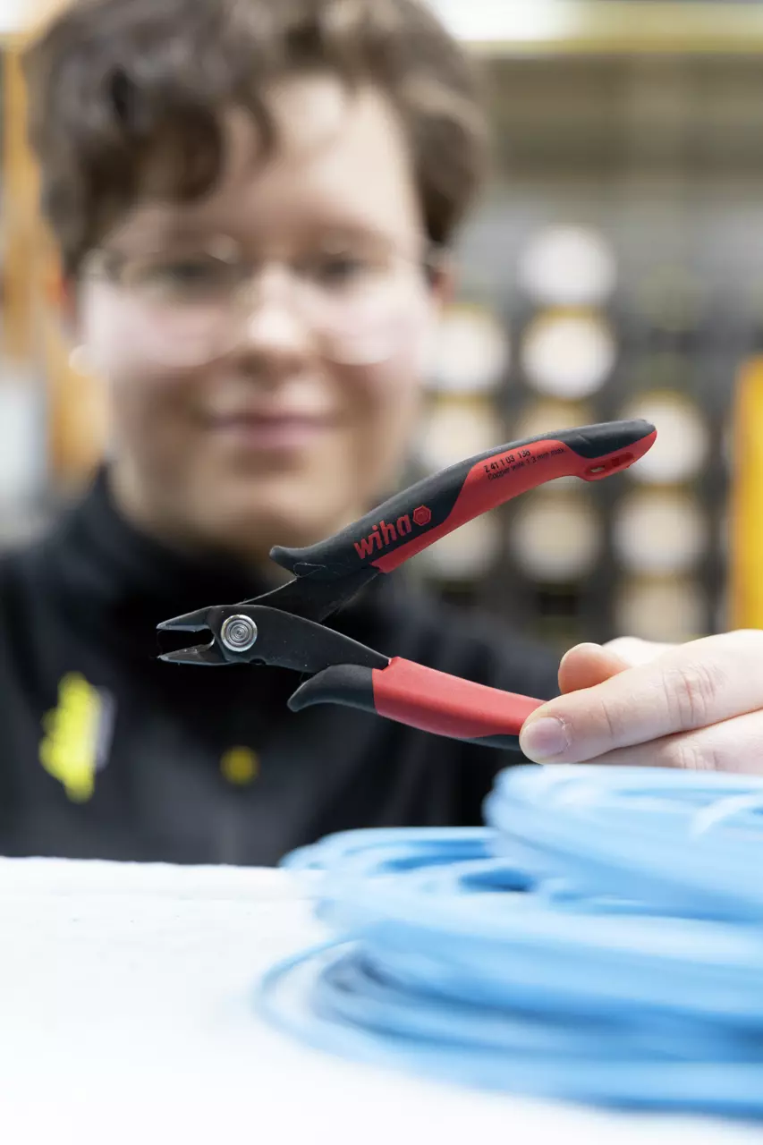 Person holding red and black electronic side cutter, focusing on tool near blue cable coil.