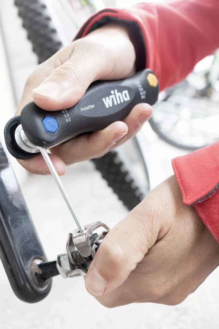 Person using a black multitool to adjust a bicycle component.