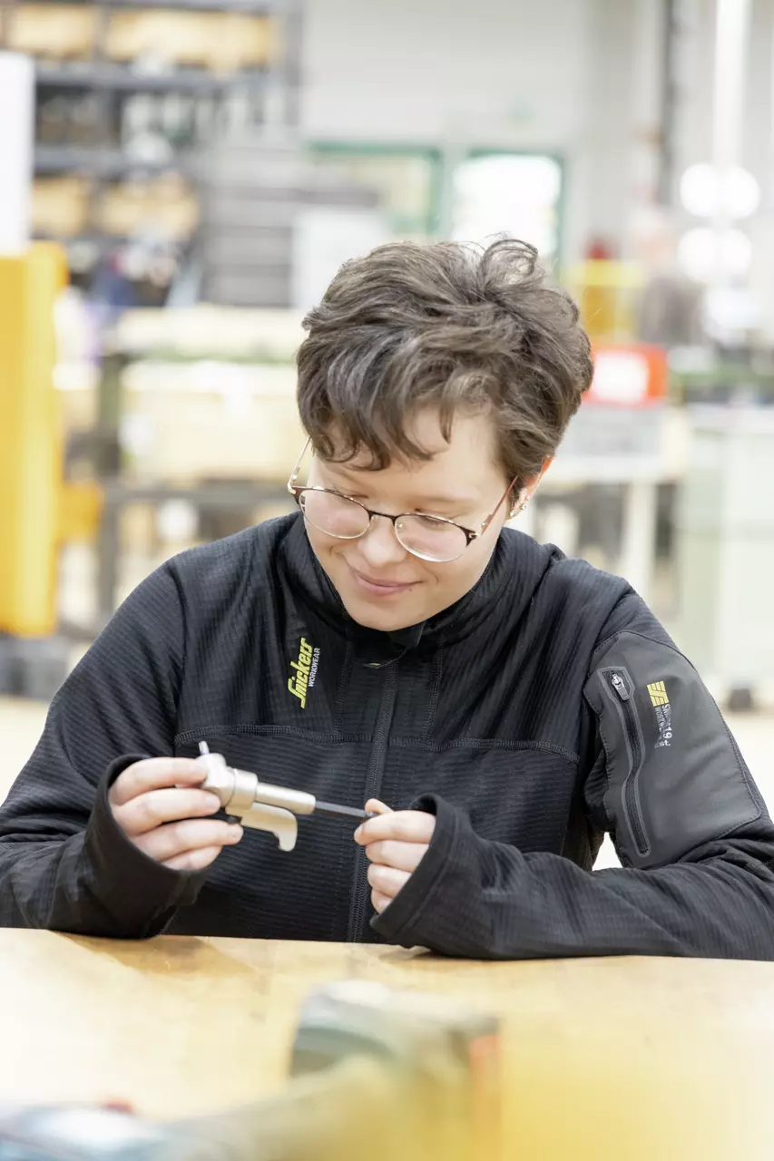 A person is holding a small metal piece and looking at it intently.