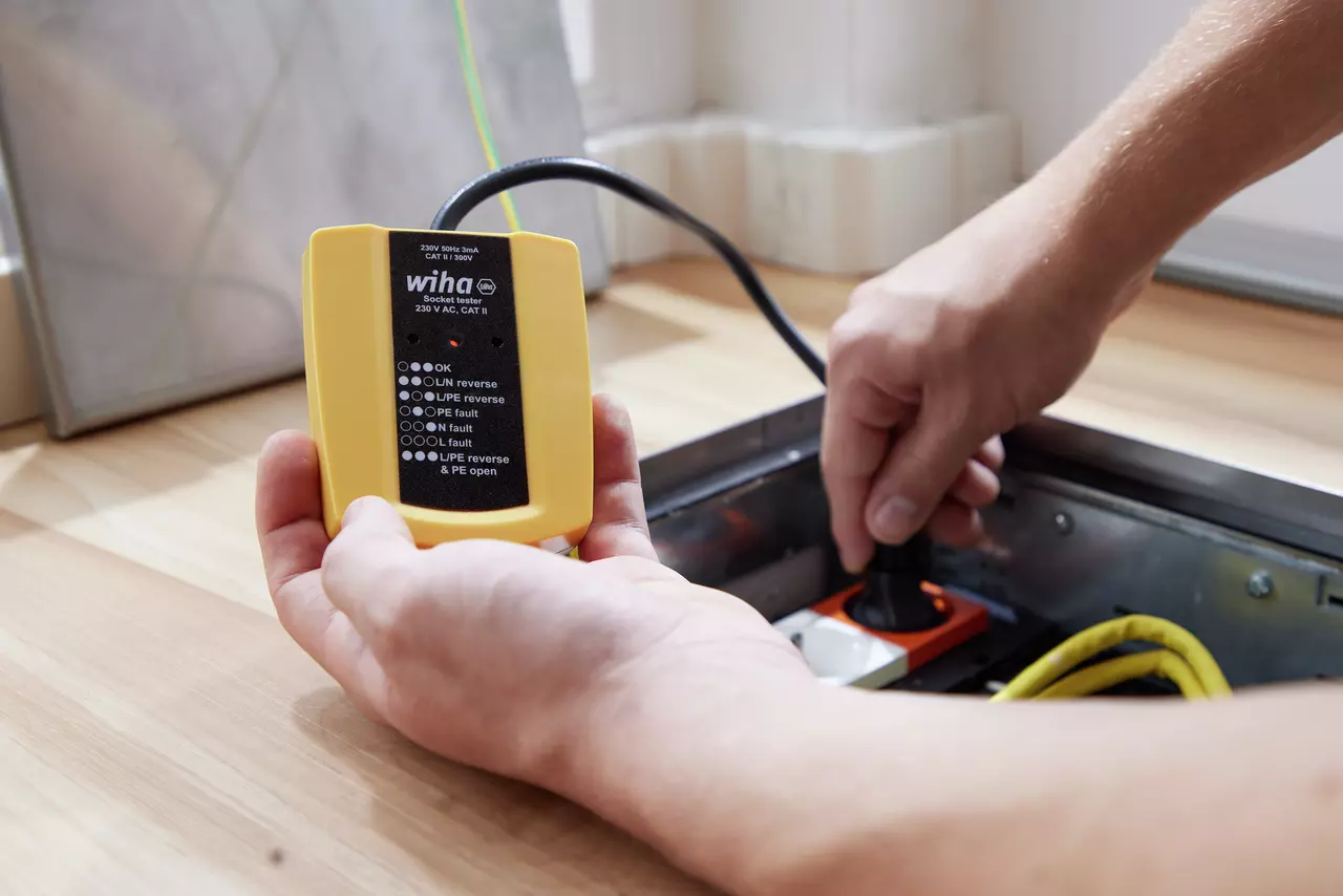 Yellow socket tester in hand, testing an electrical outlet with cable, indoors.
