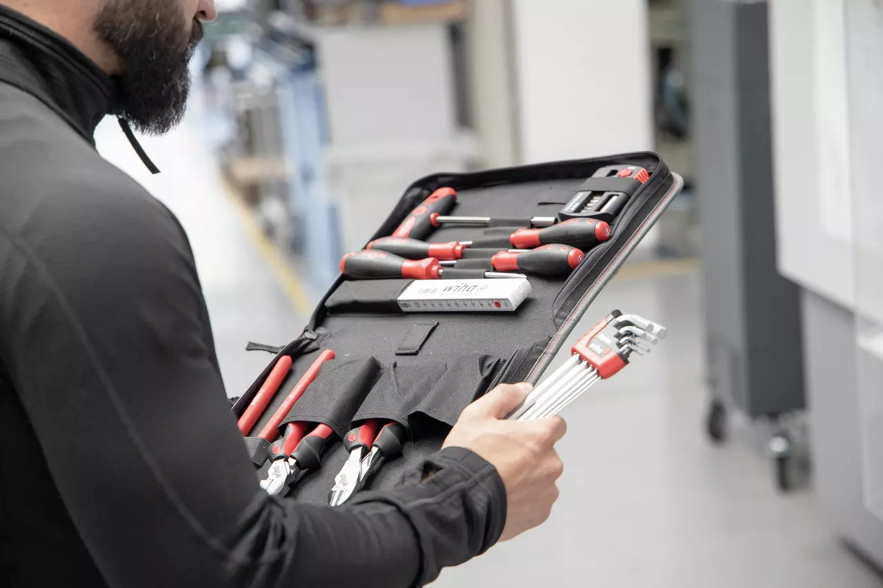 A person holding a tool set with various screwdrivers and pliers in a black case.