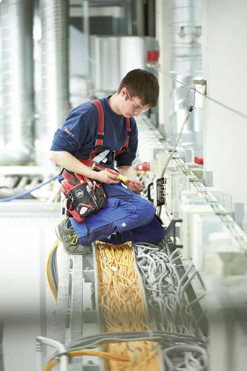 A person working with electrical cables, using a screwdriver, in an industrial setting.