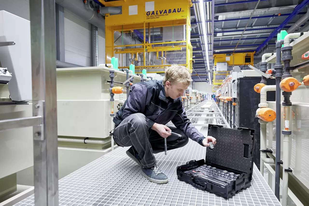Person using a socket set in an industrial setting with machinery and pipes.