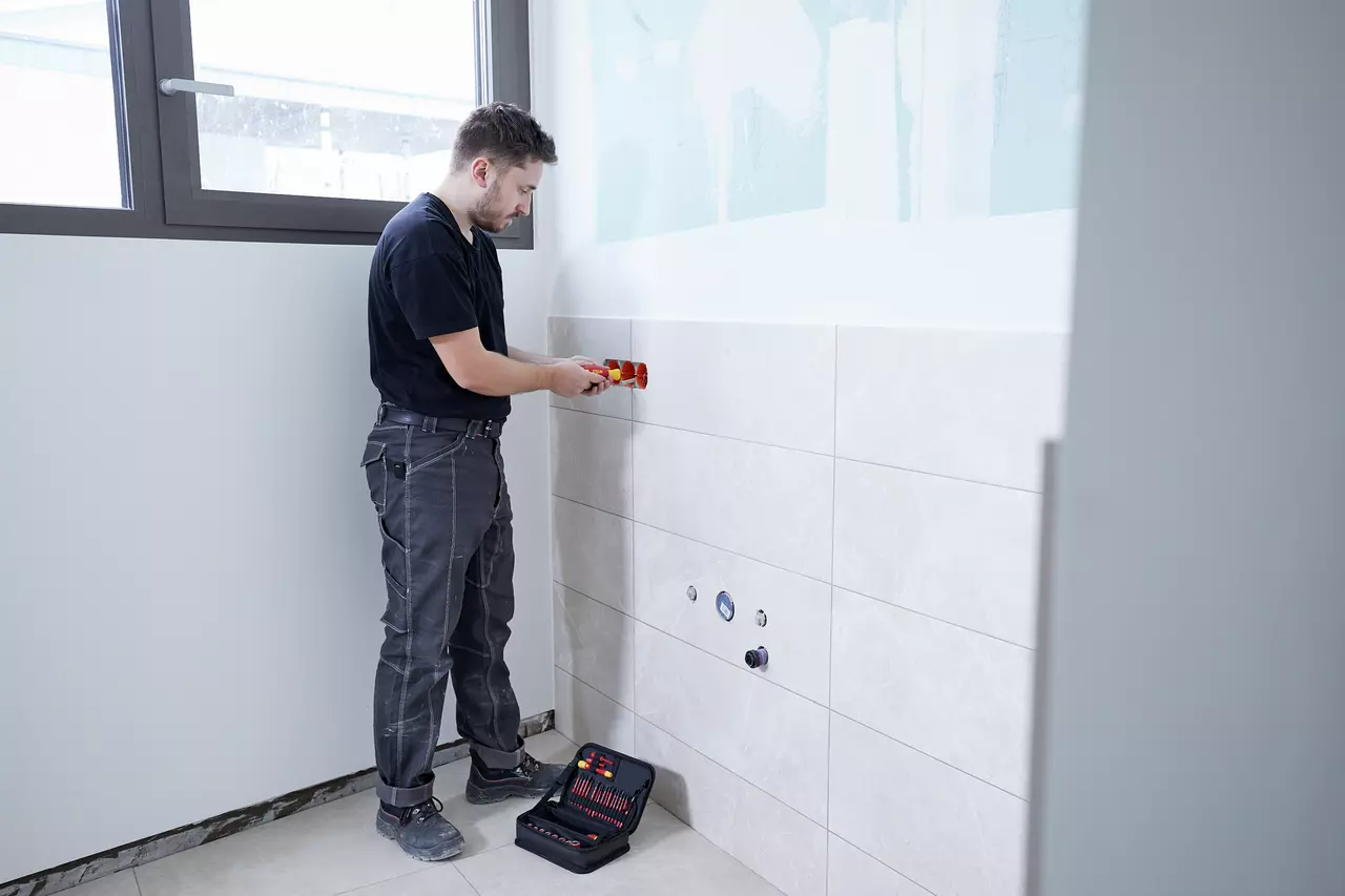A person using a screwdriver on a tiled wall in a room
