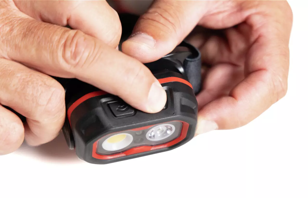 A person pressing a button on a black and red headlamp.