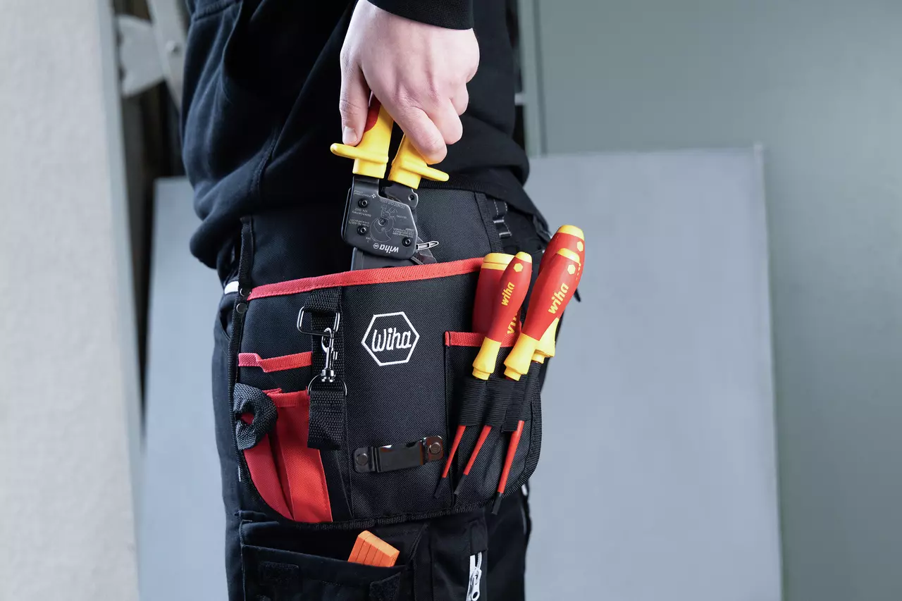 Person holding yellow cable cutter, tool belt with screwdrivers