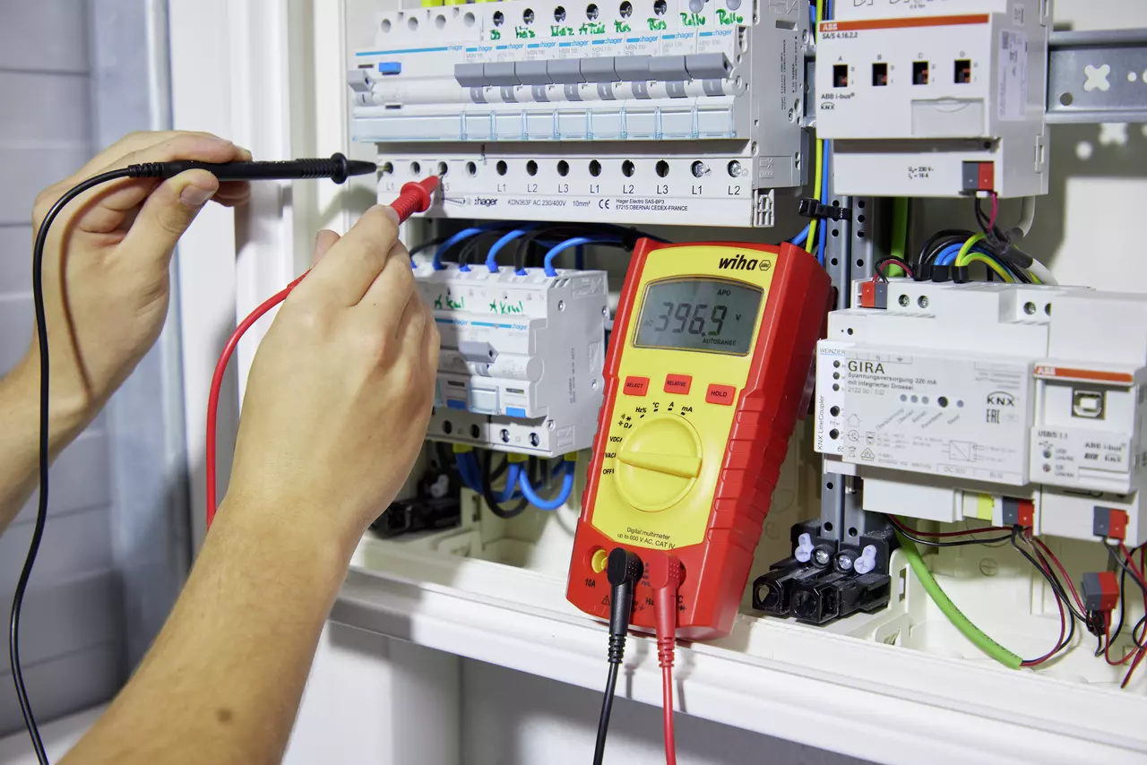 Person using a digital multimeter in an electrical cabinet.
