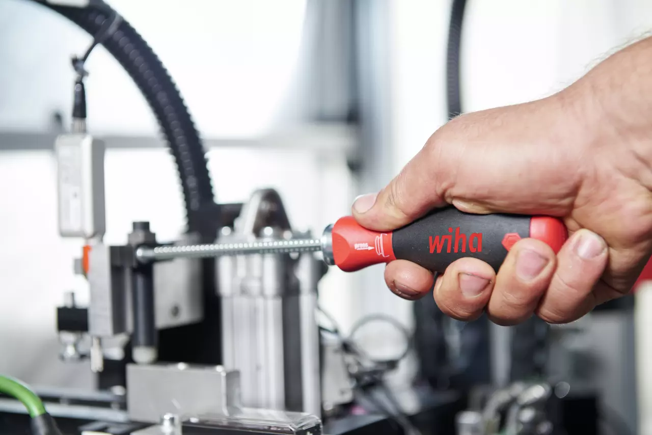 A person uses a screwdriver on a mechanical device, holding a red and black handle.