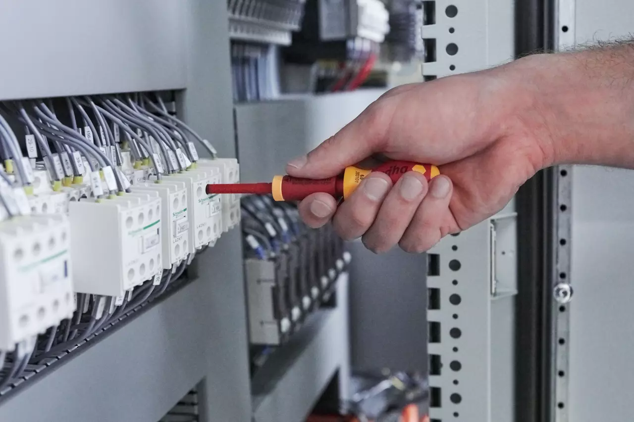 A person using an insulated screwdriver on an electrical panel.