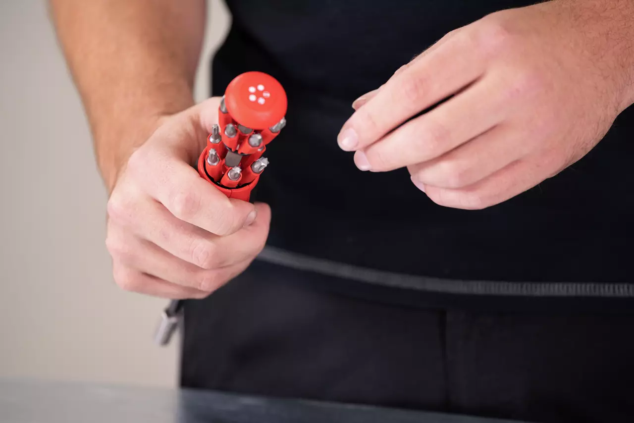 Person holding a red multi-bit screwdriver with various bits