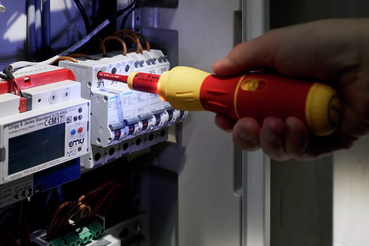 Person using a red and yellow electric screwdriver on a circuit breaker panel.