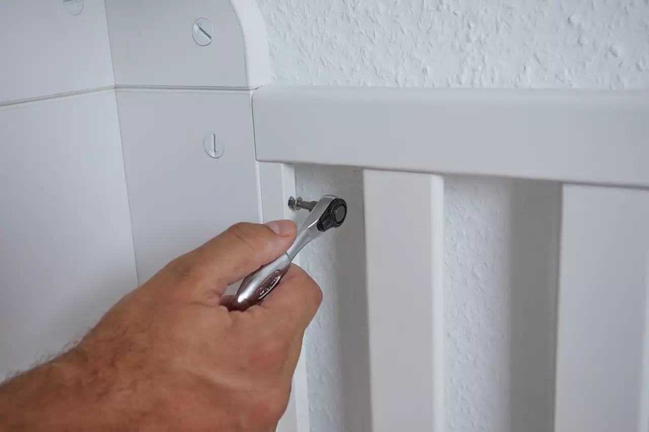 A person using a ratchet to tighten a screw on a white piece of furniture.