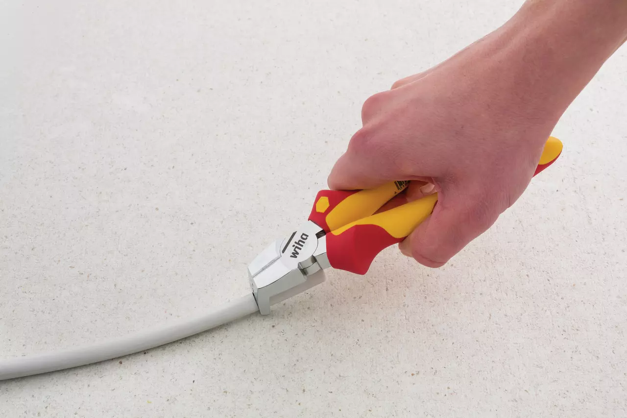 A hand using insulated pliers to strip a cable on a light surface.