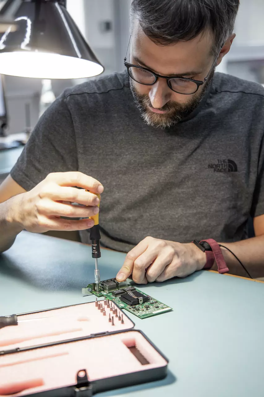 Une personne utilise un tournevis sur un circuit imprimé sous une lampe.