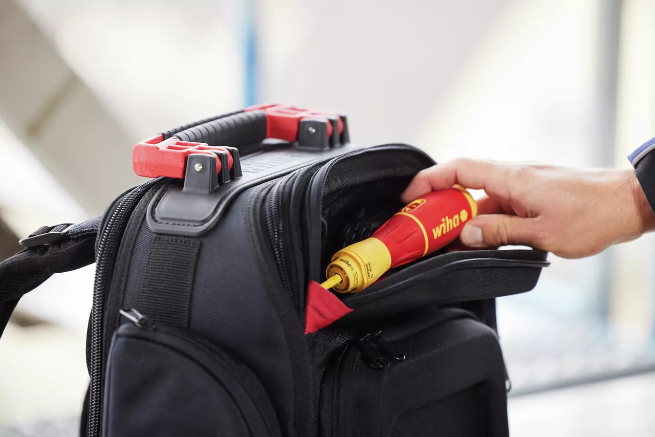 A hand placing a red and yellow screwdriver into a black tool bag.
