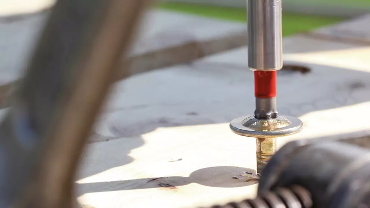 A screwdriver driving a screw into a wooden surface.