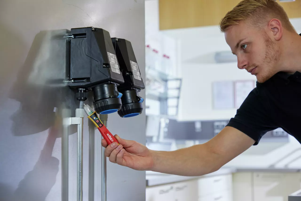 A person using a red non-contact voltage tester on a black electrical socket