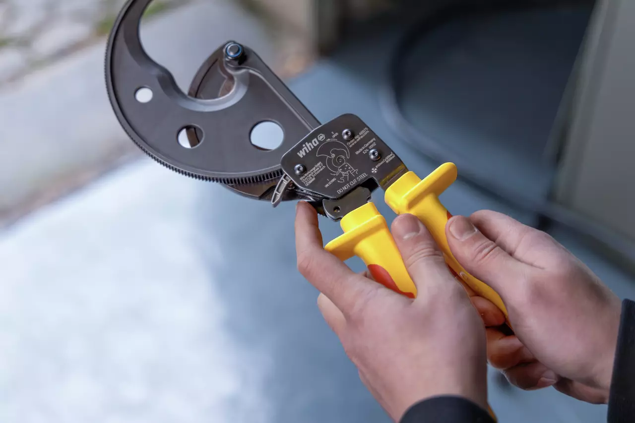 Person holding ratchet cable cutter with yellow handles.