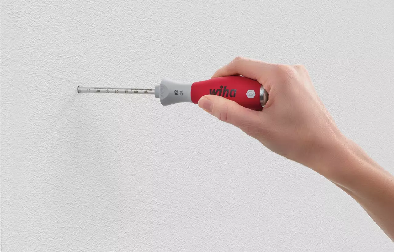Hand holding a depth gauge tool against a white wall.