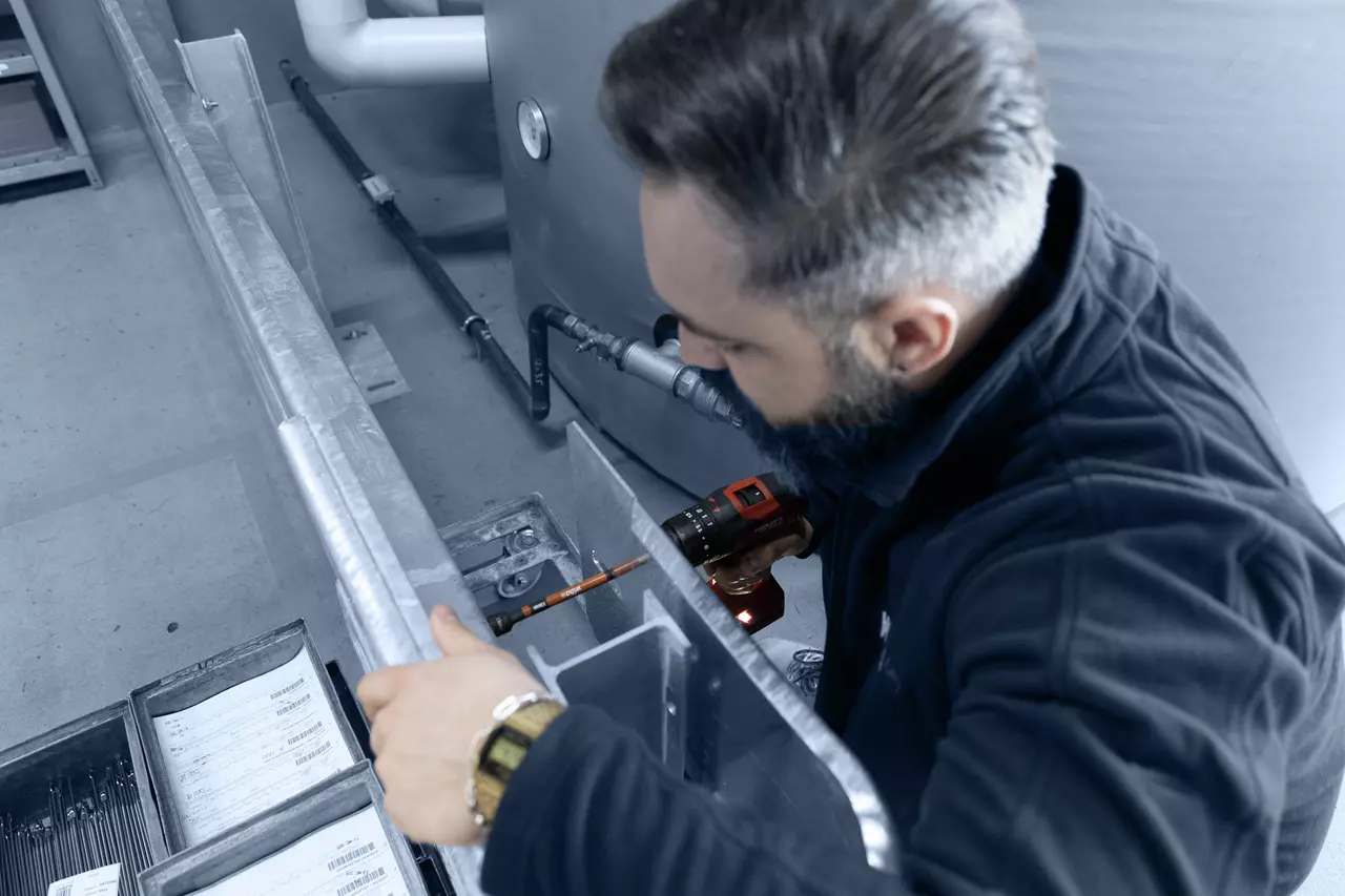 A person using a red electric screwdriver on metal structures in an industrial setting.