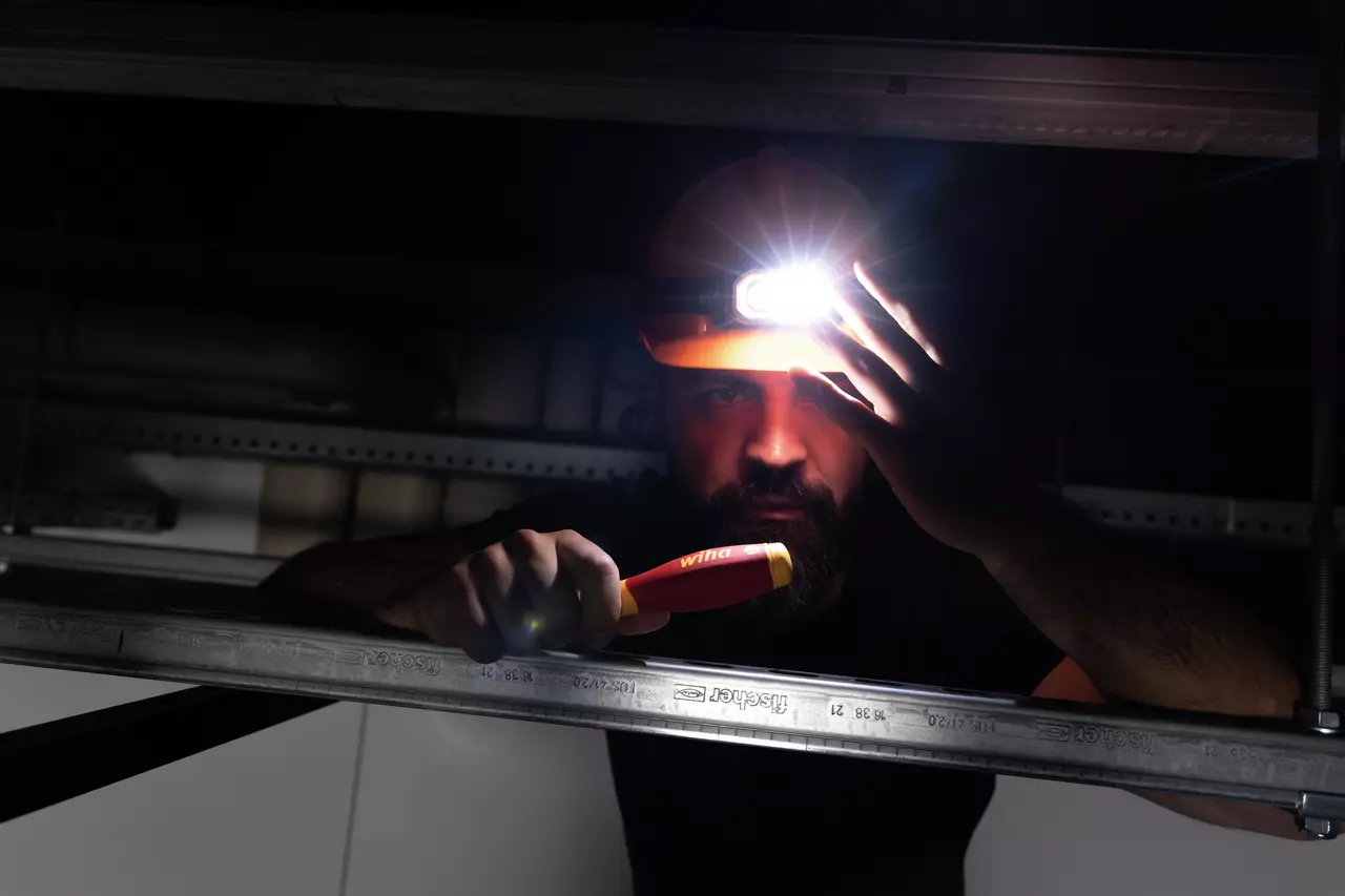 A person wearing a headlamp and holding a tool, working in a dark space.