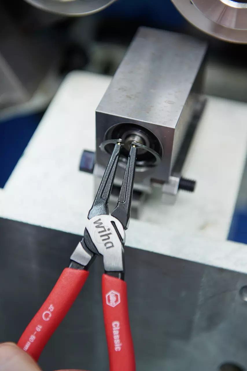 Red retaining ring pliers holding a metal retaining ring on a machine.