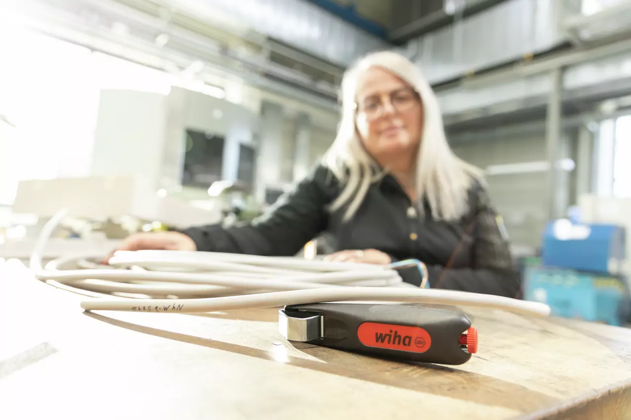 Woman in workshop with cable stripping tool on table.