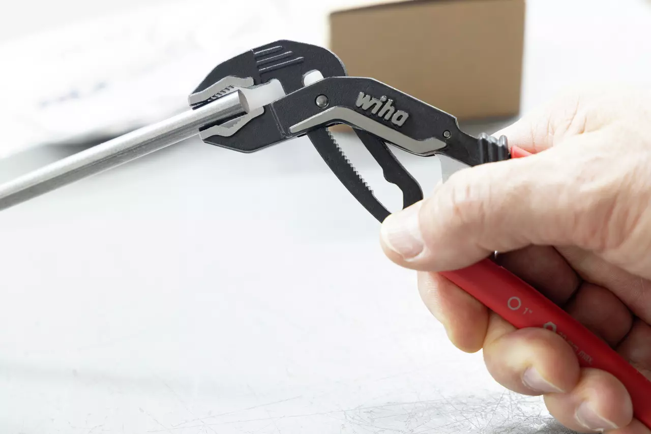 A person uses a water pump plier with red handles to grip a metal rod.