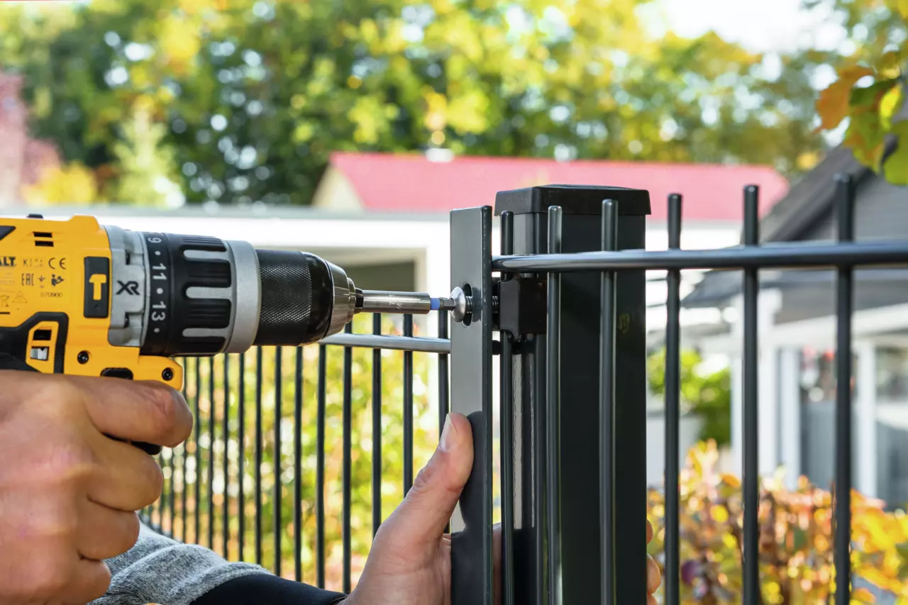 Person using a yellow drill to secure a metal fence