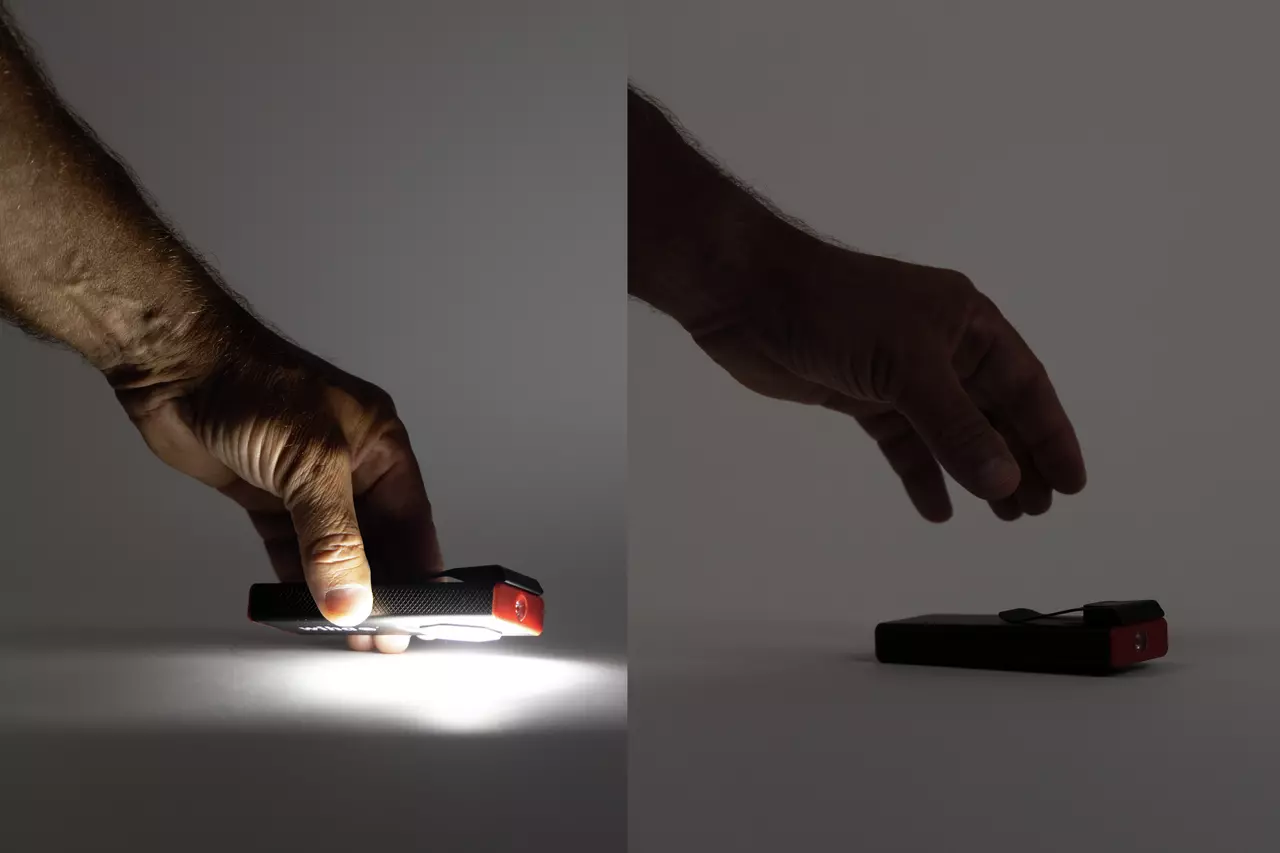 A hand holding a black and red flashlight, illuminating a surface.