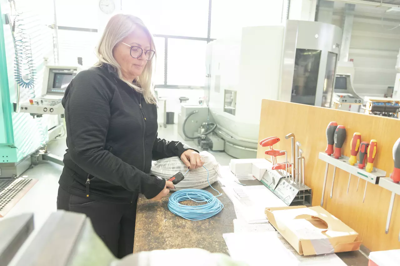 Osoba pracuje s nástrojem na modrém drátu v dílně