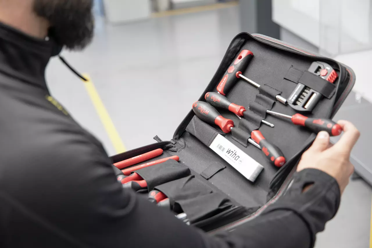 A person holding an open tool set with red and black screwdrivers and bits in a black case.
