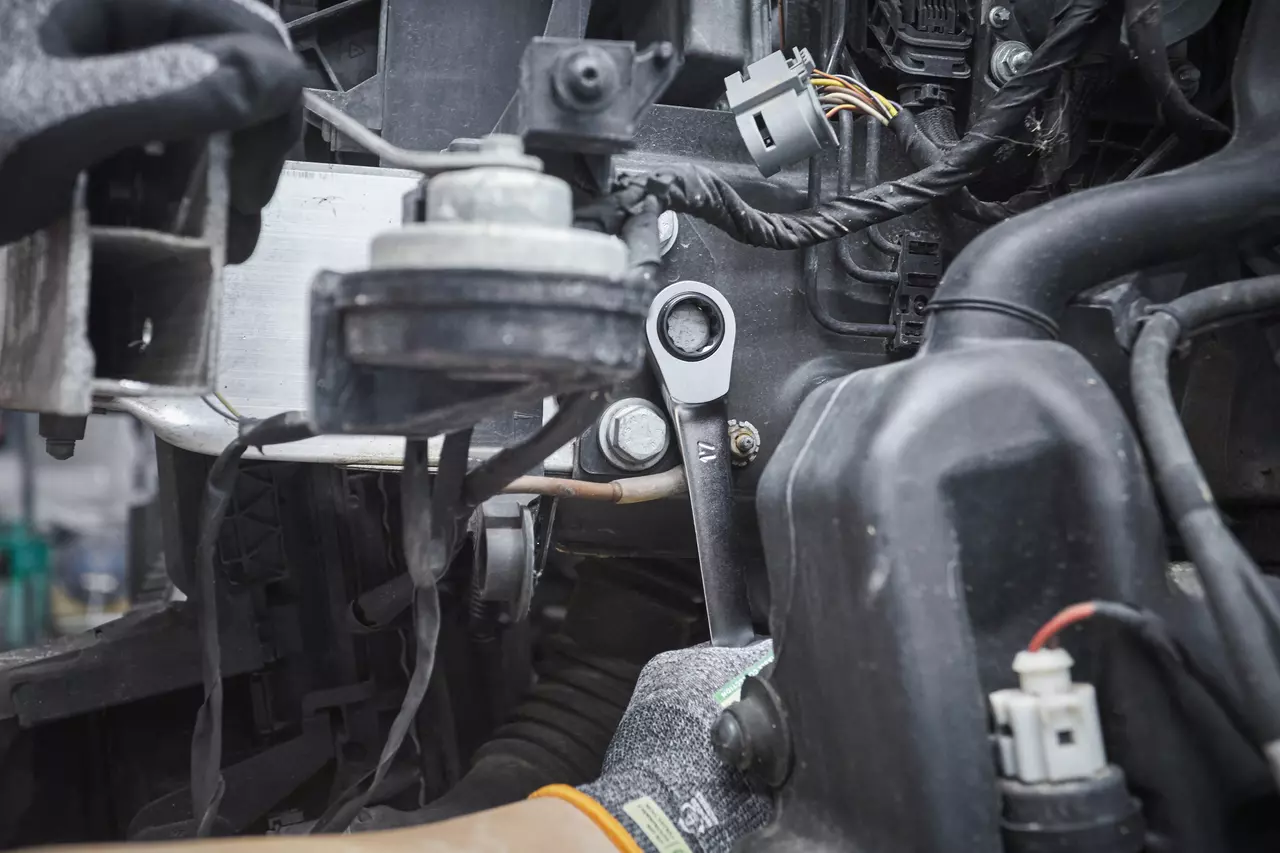 Une personne utilise une clé à cliquet pour travailler sur un moteur de voiture.