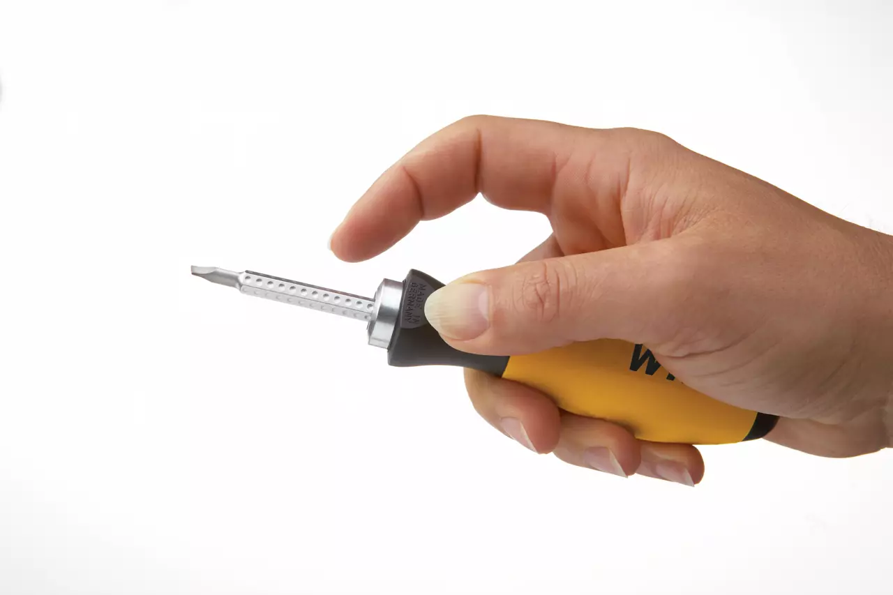 A hand holding a yellow and black screwdriver with a metal tip.