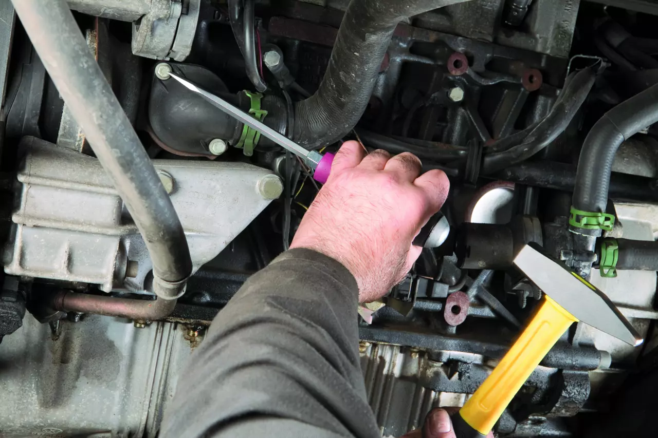 Person working on an engine with screwdriver and hammer