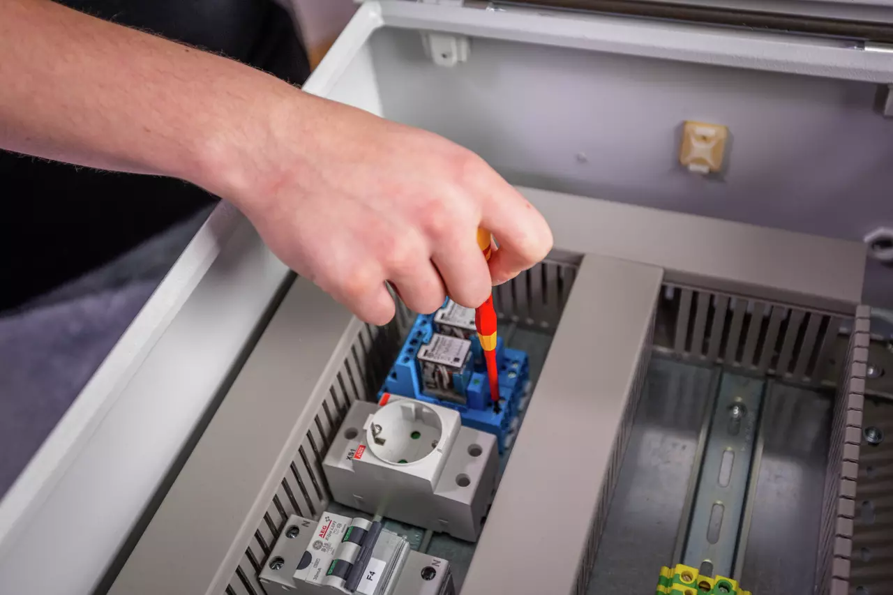 A person uses a fine screwdriver on an electrical component inside a control panel.