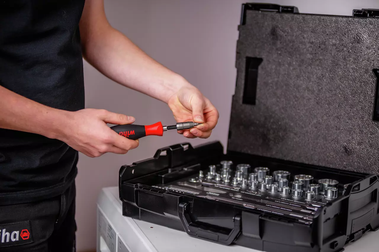 Person using a screwdriver with a socket set in an open case on a table.