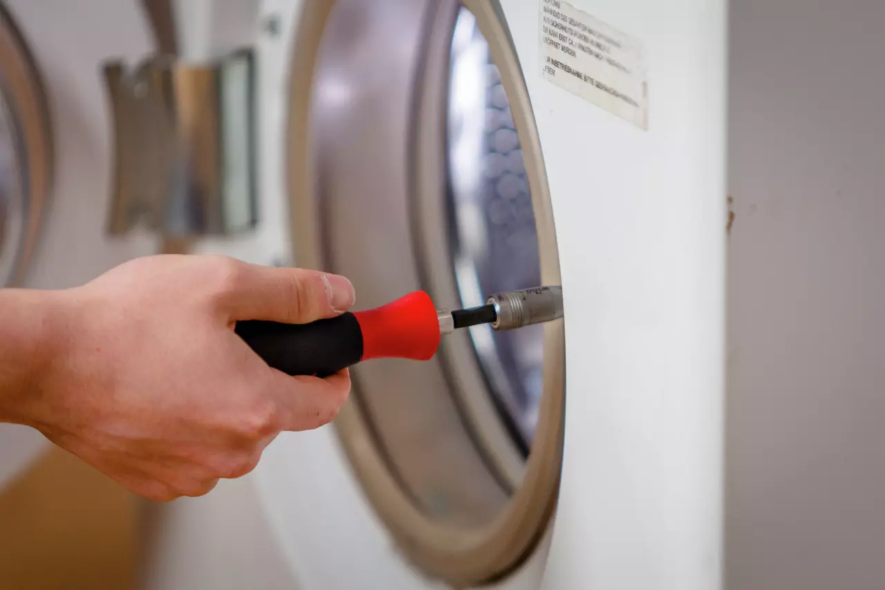 A person using a screwdriver on the door of a washing machine.