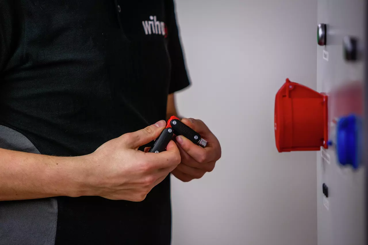 A person holding a black and red universal key near a control panel.