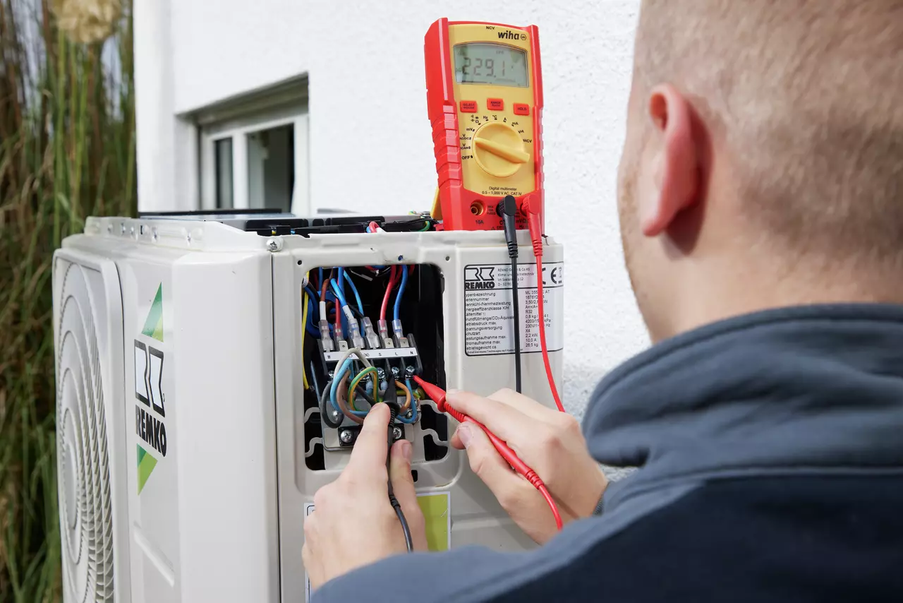 En person använder en digital multimeter för att testa en luftkonditionerings elektriska anslutningar.