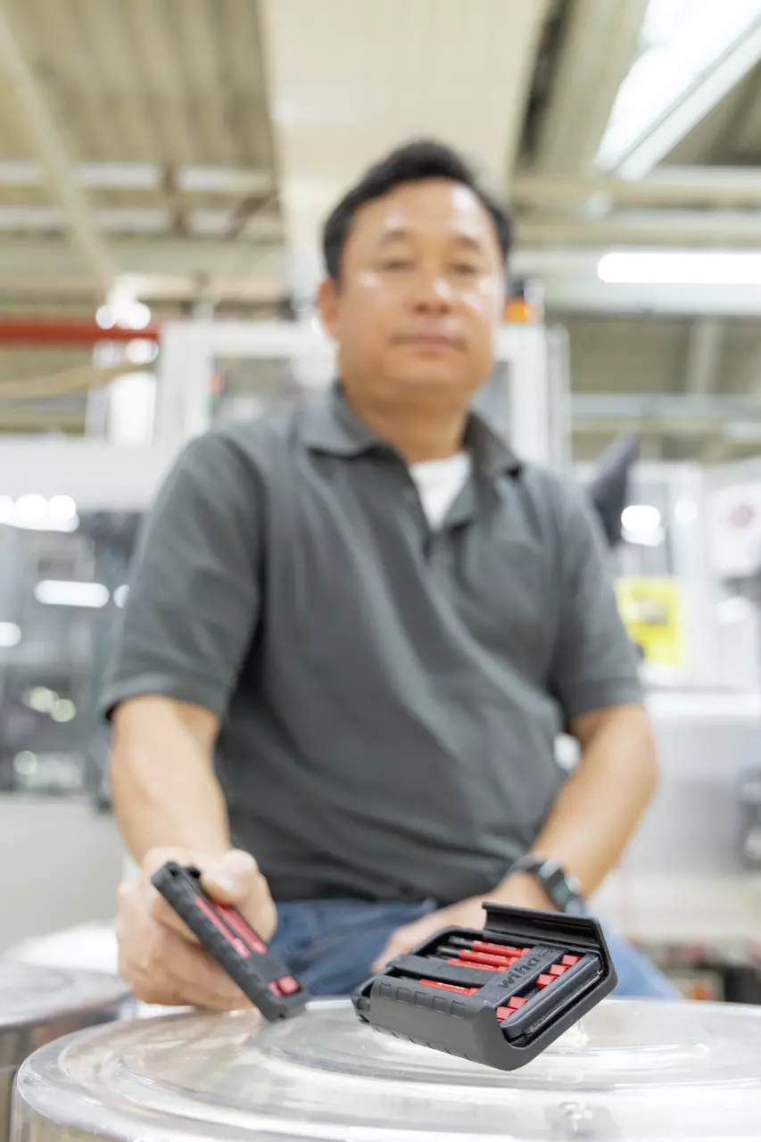 Blurry person in workshop holding black tool case with red screwdriver handles.