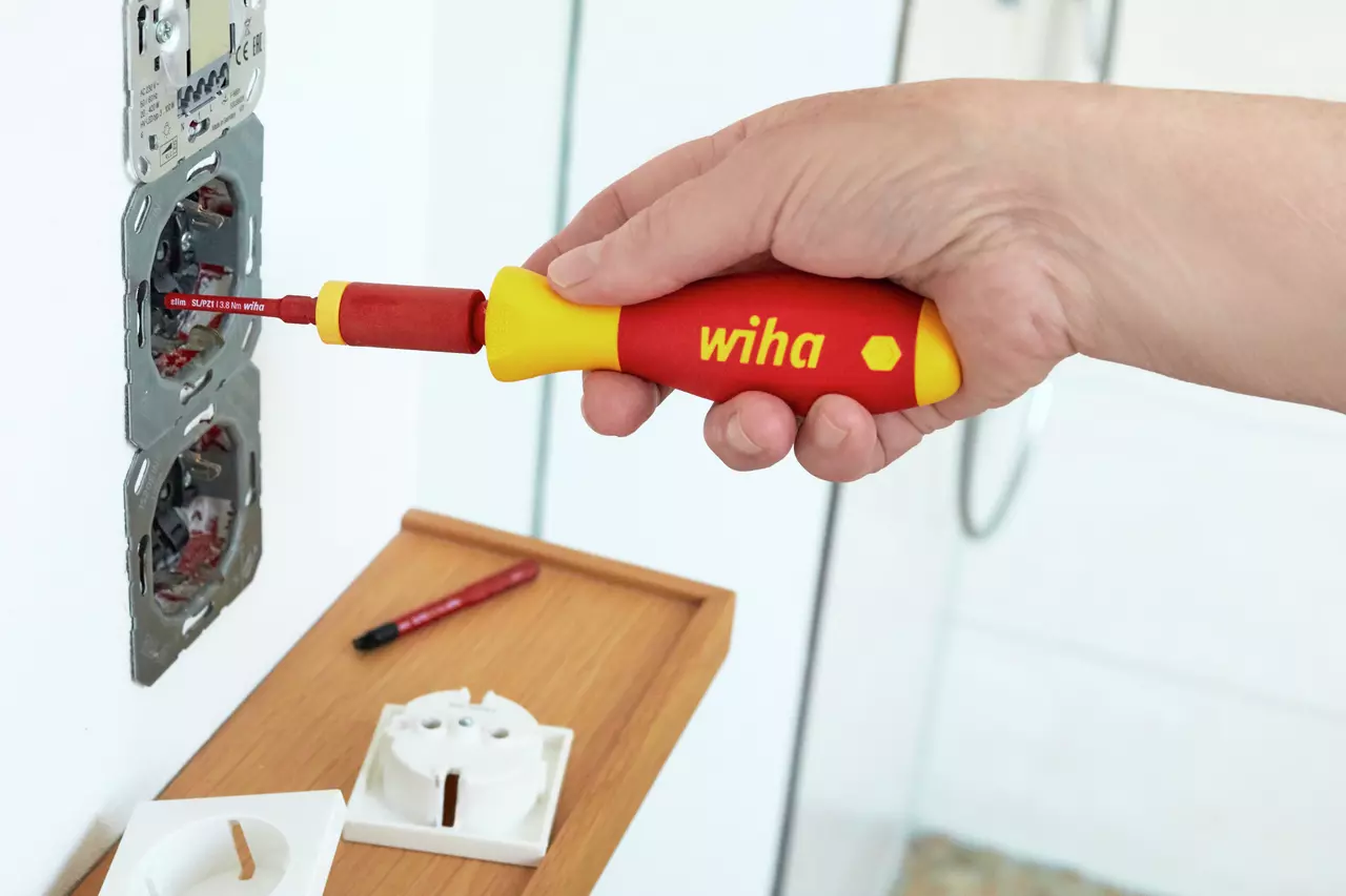 A person uses a red and yellow screwdriver on an electrical socket.