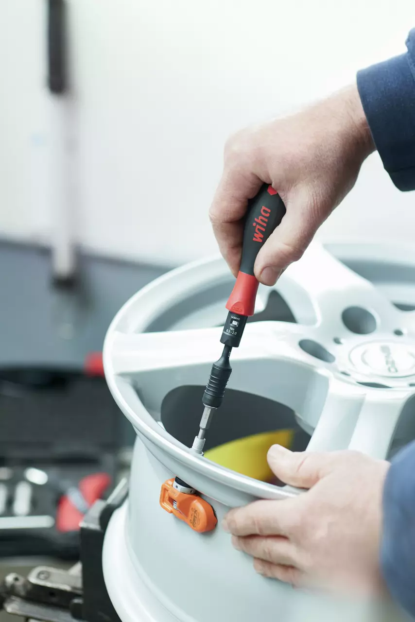 A person using a torque screwdriver on a car wheel rim.