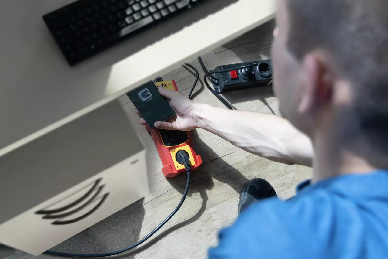 Person bruger en smartphone til at scanne en ladestation under et skrivebord.