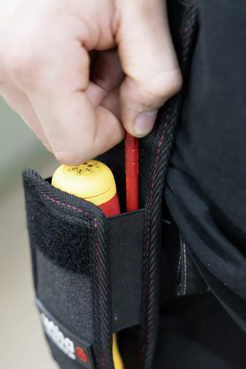 Person placing a tool into a black belt pouch with red stitching.