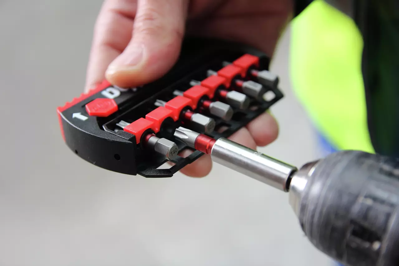 Hand holding a set of screwdriver bits with one attached to a drill.