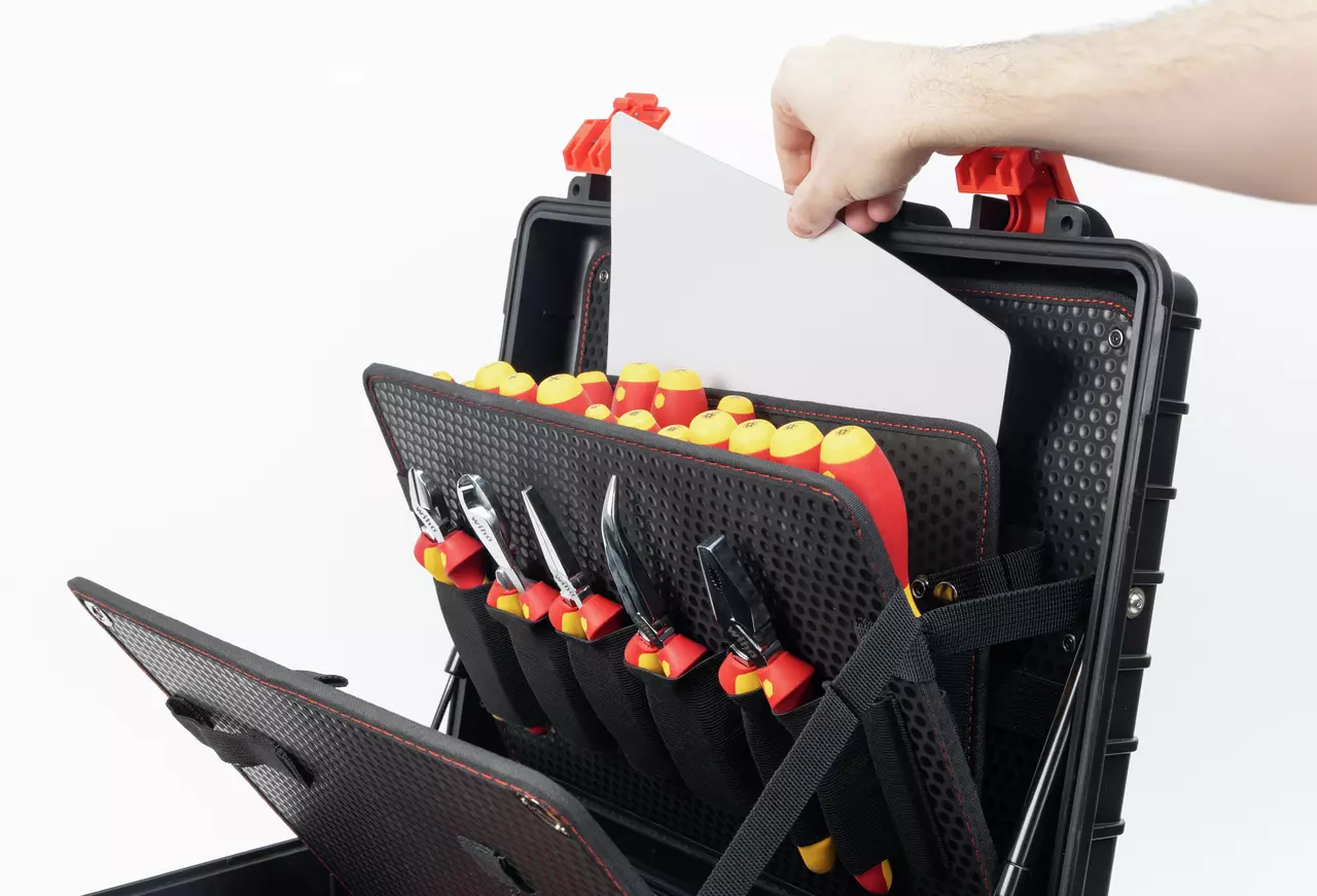 A hand placing a document into a tool case with organized screwdrivers and pliers.